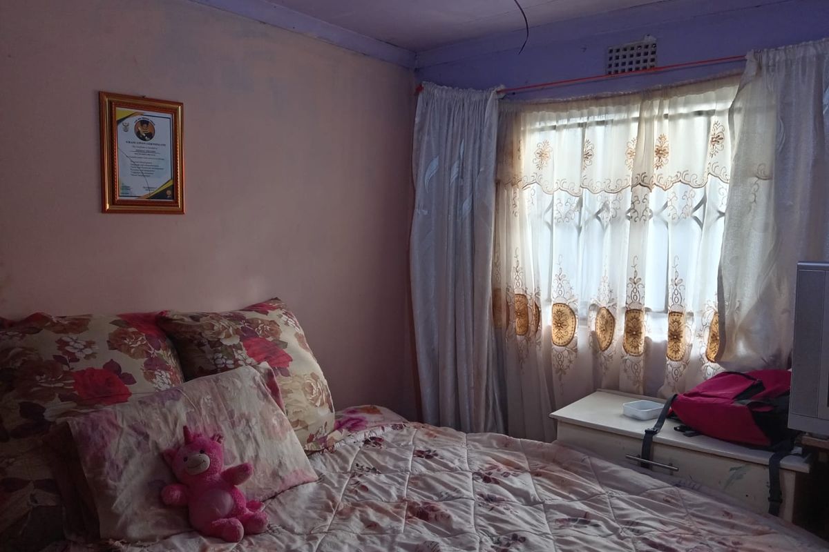 A bedroom featuring a window with security bars and curtains, showing signs of wear on the walls and ceiling.
