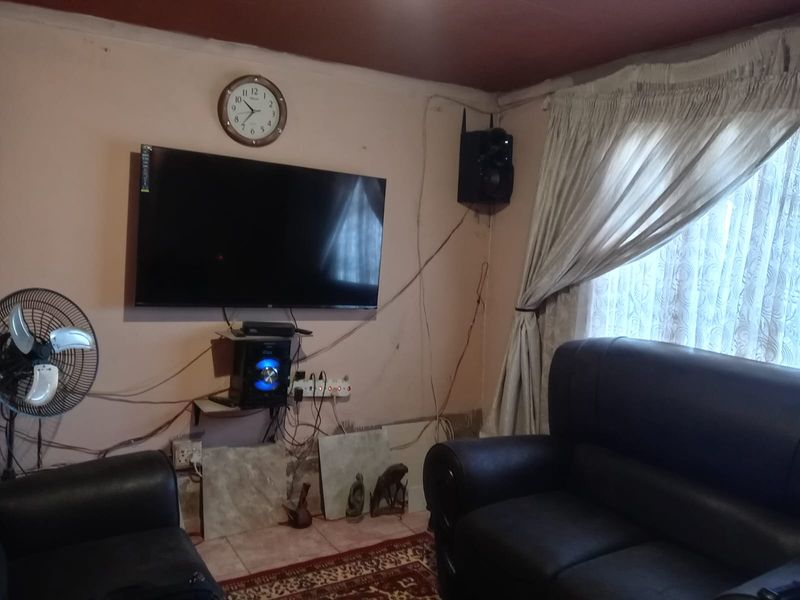 A living room area featuring a wall-mounted television, tiled flooring, and window treatments.