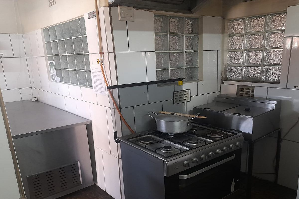 A functional commercial-style kitchen area featuring stainless steel appliances, a gas stove, and glass block windows for natural light.