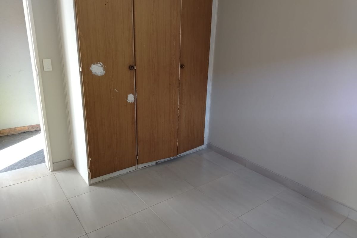A bedroom featuring built-in wooden wardrobes with visible wear and tiled flooring, offering a blank canvas for potential updates.
