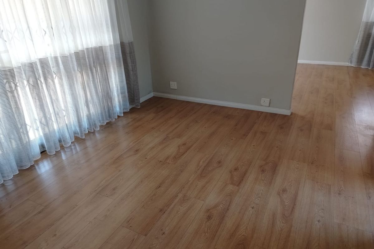 A bright, empty living area featuring modern wood-look laminate flooring, neutral wall tones, and clean skirting boards.