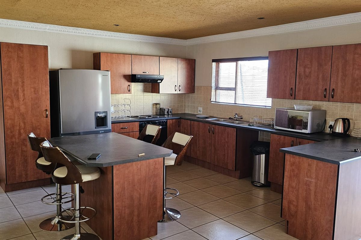 Spacious kitchen featuring wood-finish cabinetry, dark countertops, a central island with breakfast bar seating, and tiled flooring.