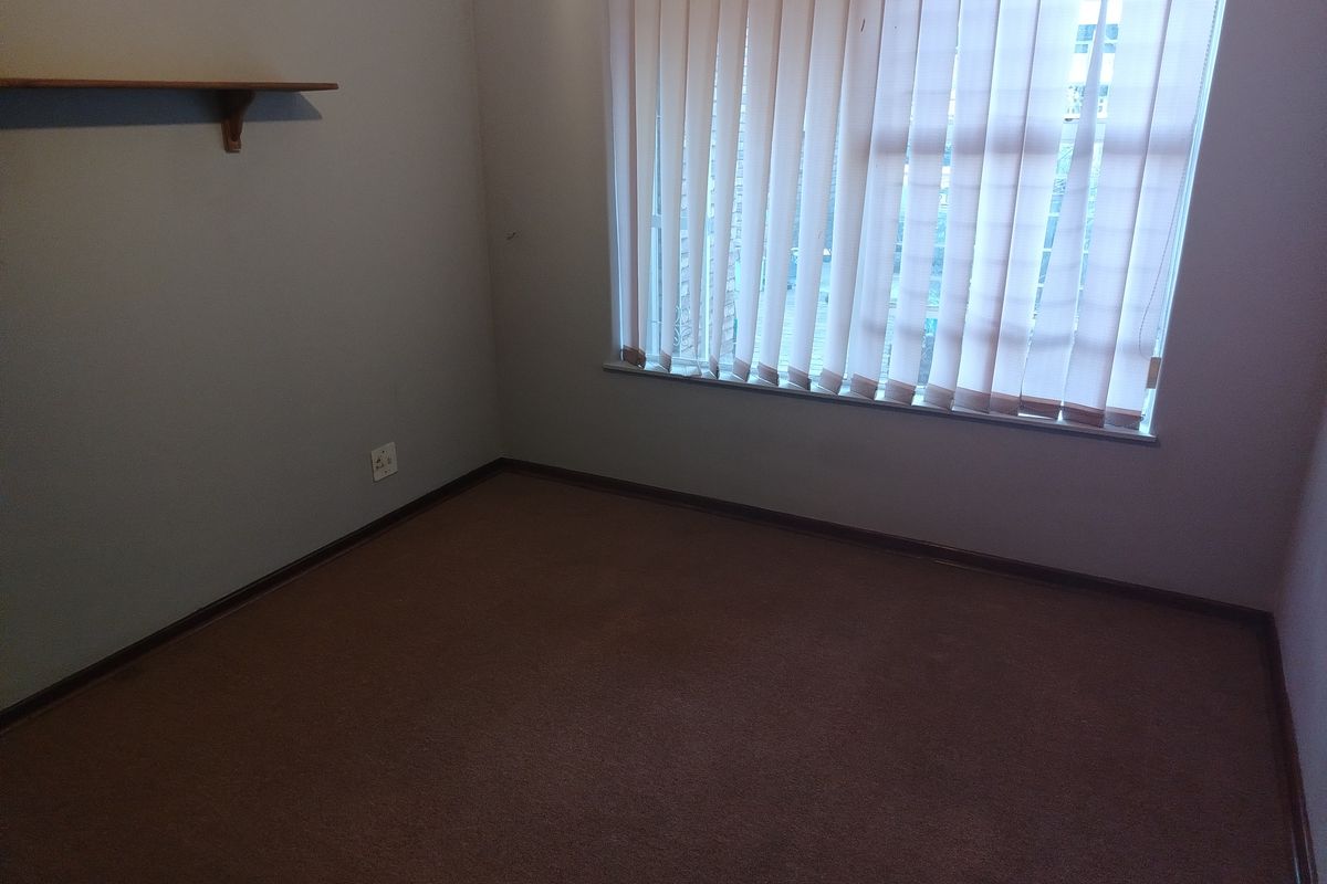 A vacant bedroom featuring neutral wall tones, brown carpeting, and vertical window blinds.