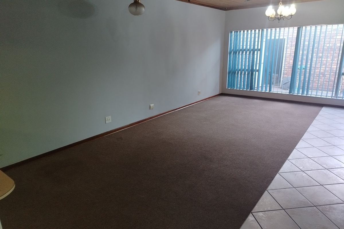 Spacious living area featuring a combination of carpet and tiled flooring, large windows with vertical blinds, and a wood-paneled ceiling.