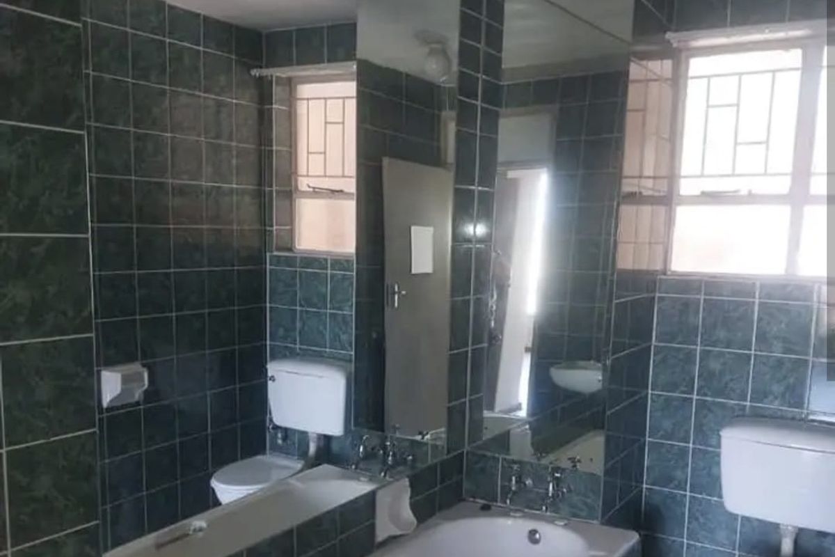 A dated bathroom featuring dark green wall tiles, a built-in bathtub, and a standard toilet suite with integrated mirror paneling.