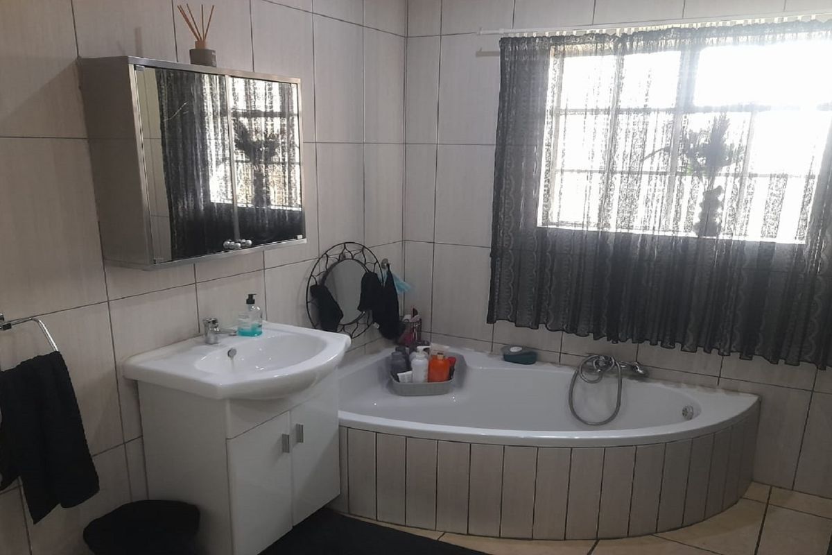 A functional bathroom featuring a corner bathtub, a vanity basin with storage, and full-height wall tiling.
