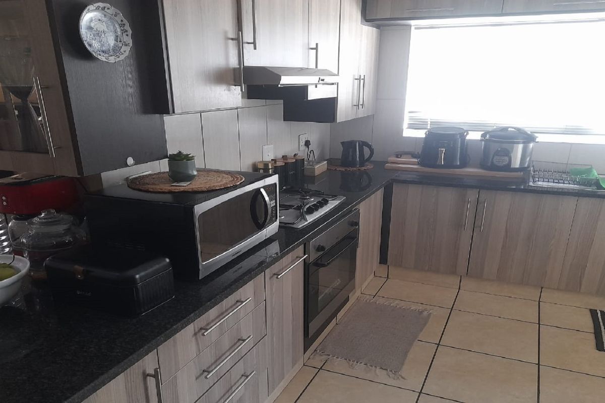 A functional kitchen featuring wood-grain cabinetry, dark granite countertops, a built-in oven, gas hob, and an extractor fan.