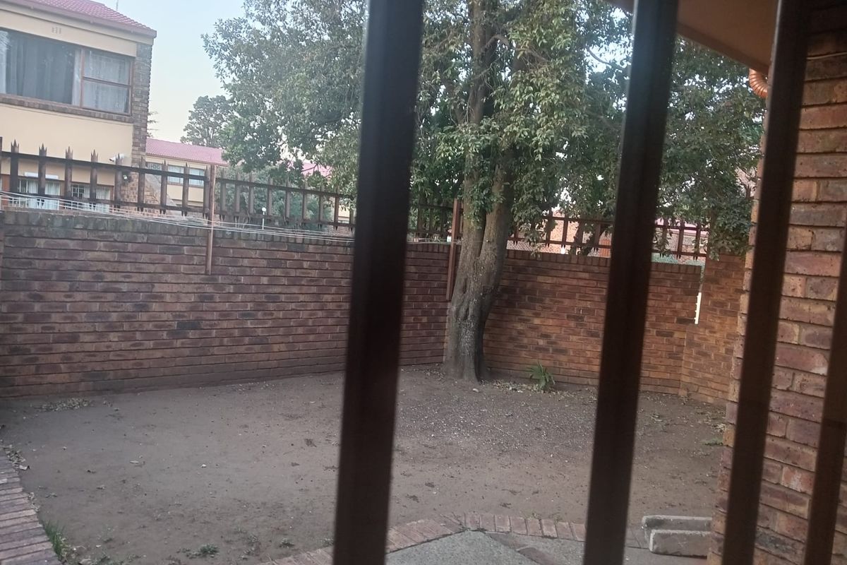 A private rear garden area featuring brick boundary walls and a mature tree, viewed from behind security bars.