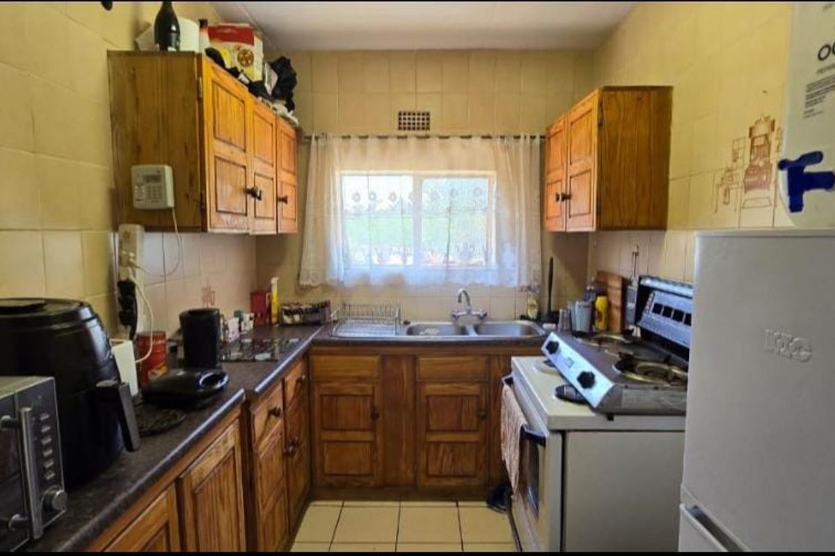 A compact kitchen featuring wooden cabinetry, tiled walls, and a double basin sink, offering a functional layout with potential for modernization.