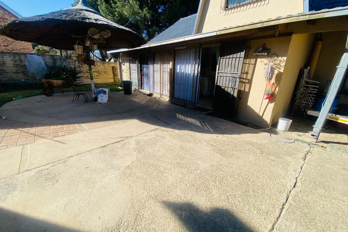 Rear exterior view of the property featuring a concrete patio area, security gates, and a thatched umbrella structure.