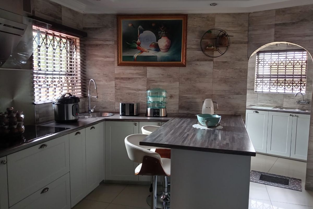 Modern kitchen featuring light-toned cabinetry, wood-look tiled backsplash, integrated breakfast bar, and a separate scullery area with additional sink and storage.