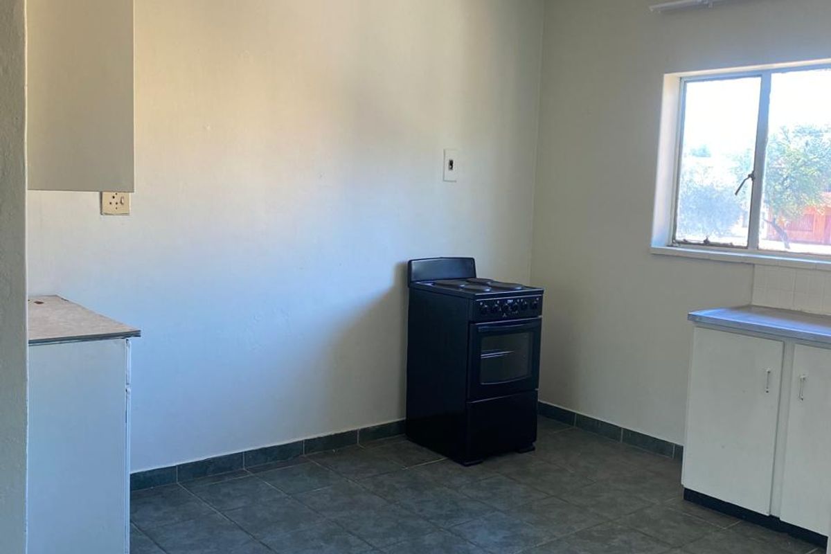 A basic kitchen area featuring tiled flooring, simple white cabinetry, and a freestanding stove, offering a functional space ready for modernization.