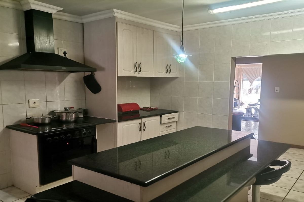 A functional kitchen featuring dark granite countertops, built-in cabinetry, a black extractor fan, and a central island with a breakfast bar.