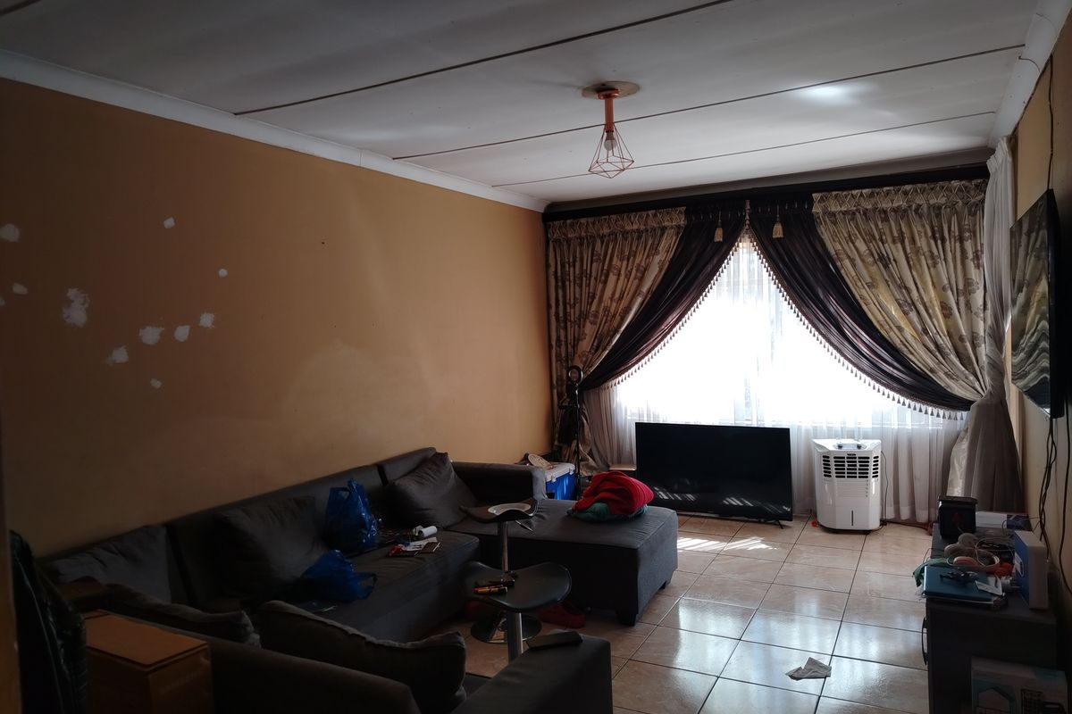 A living room featuring tiled flooring and a large window with curtain treatments, requiring cosmetic updates to the walls and ceiling.