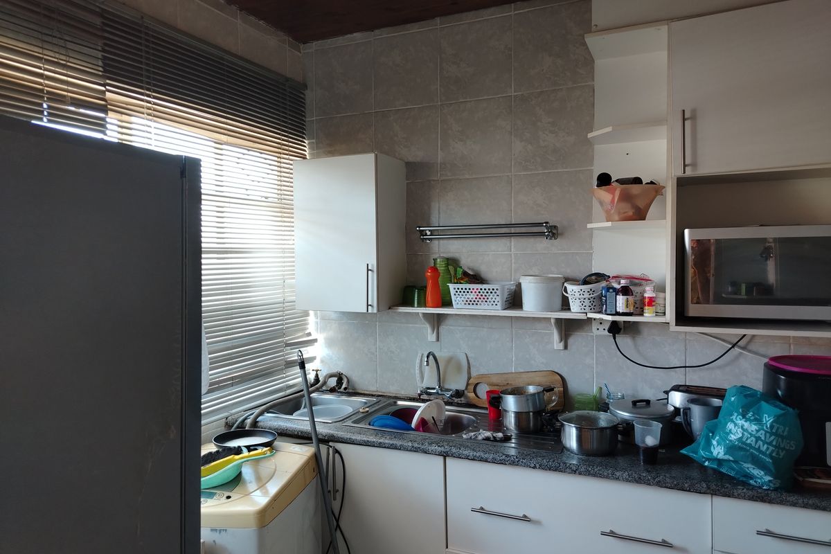 A compact kitchen featuring white cabinetry, granite-look countertops, a stainless steel sink, and tiled backsplash, with integrated space for laundry appliances.