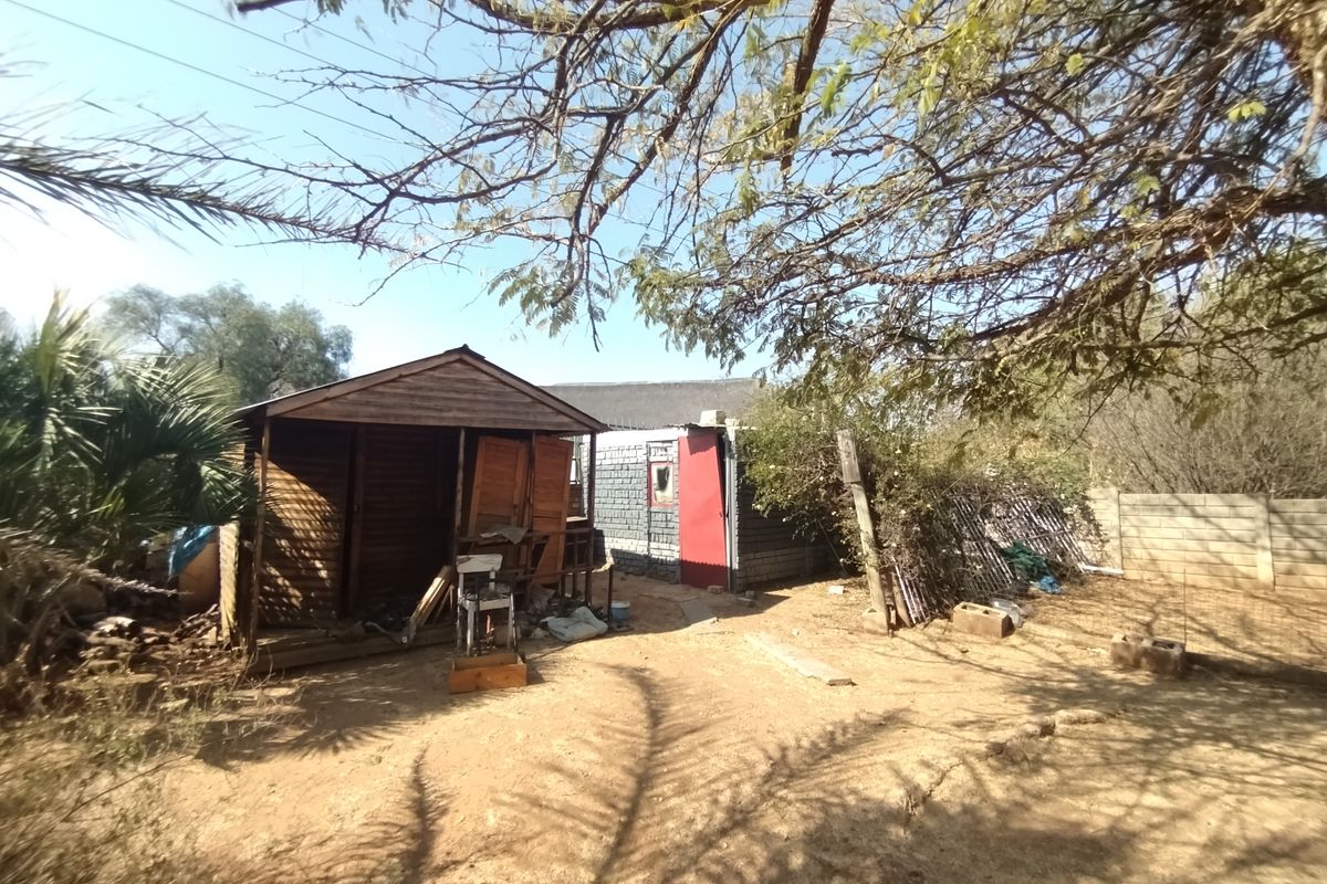 A view of the rear yard featuring a weathered timber shed and a secondary structure with masonry walls and a red door.