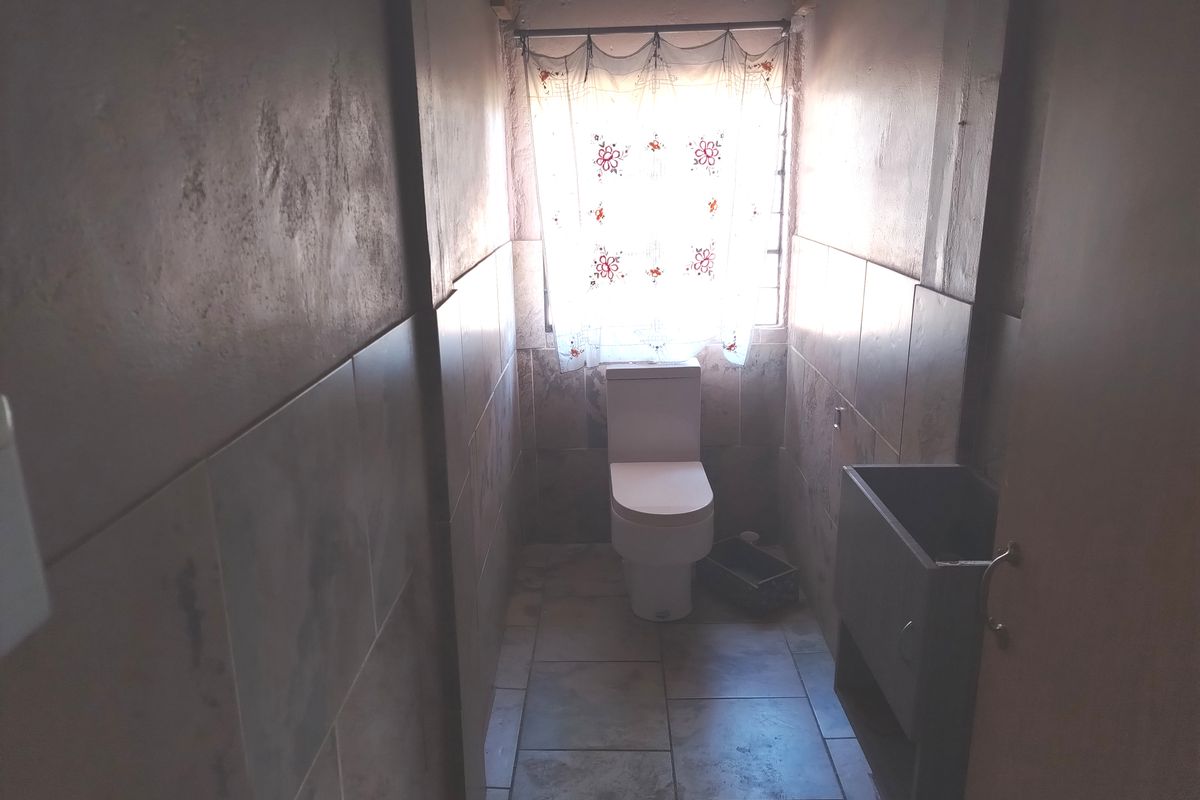 A compact bathroom featuring tiled walls and flooring, a standard toilet, and a small vanity unit, currently requiring finishing touches to the ceiling.