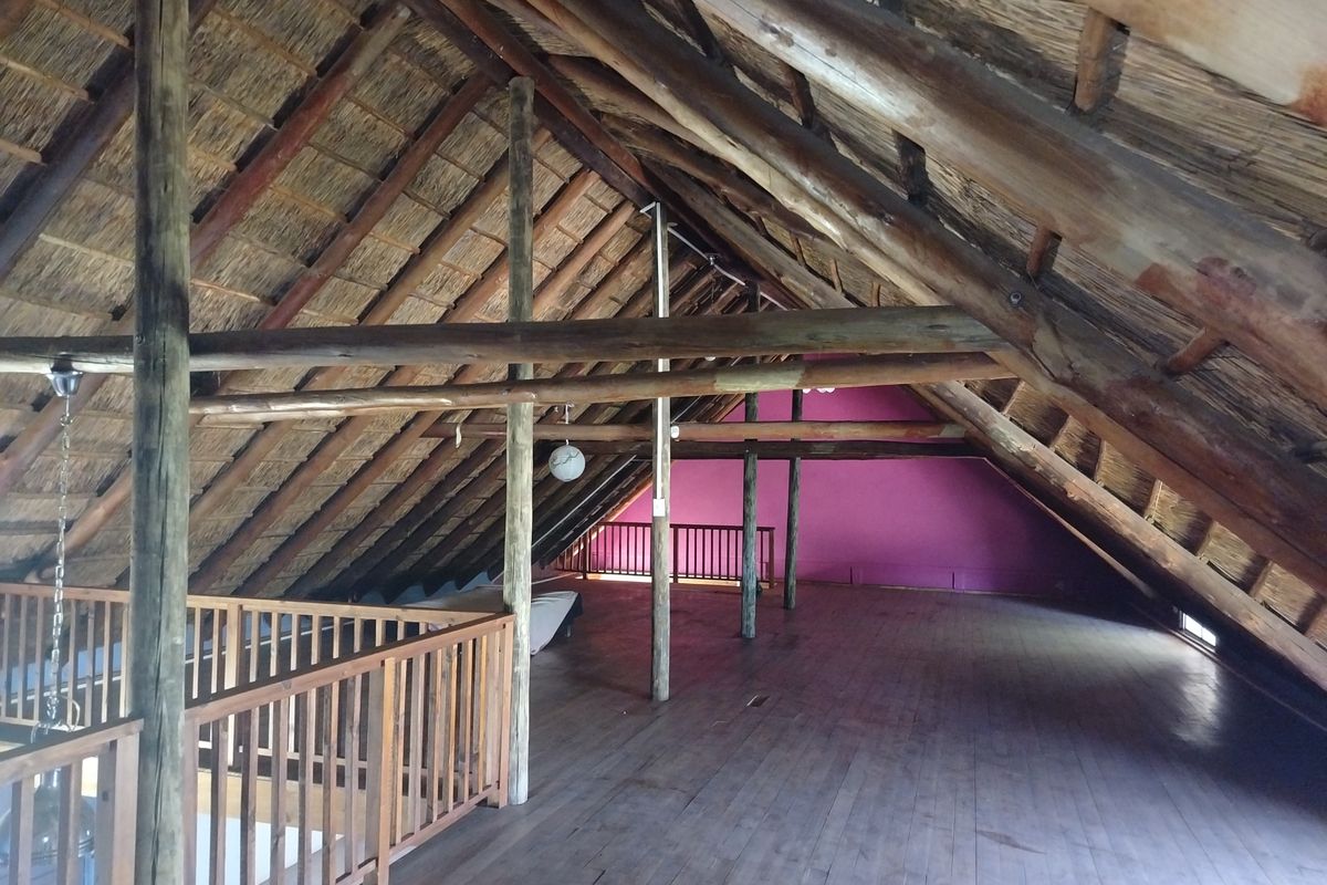 Spacious attic loft area featuring exposed timber roof trusses, a traditional thatched roof, and wooden balustrades overlooking the lower level.