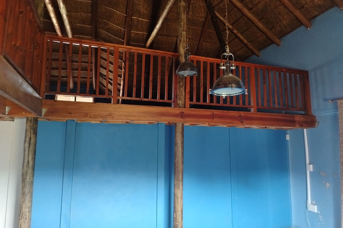 Interior view of a living area featuring a high thatched roof, exposed timber beams, and a wooden mezzanine level with a balustrade.