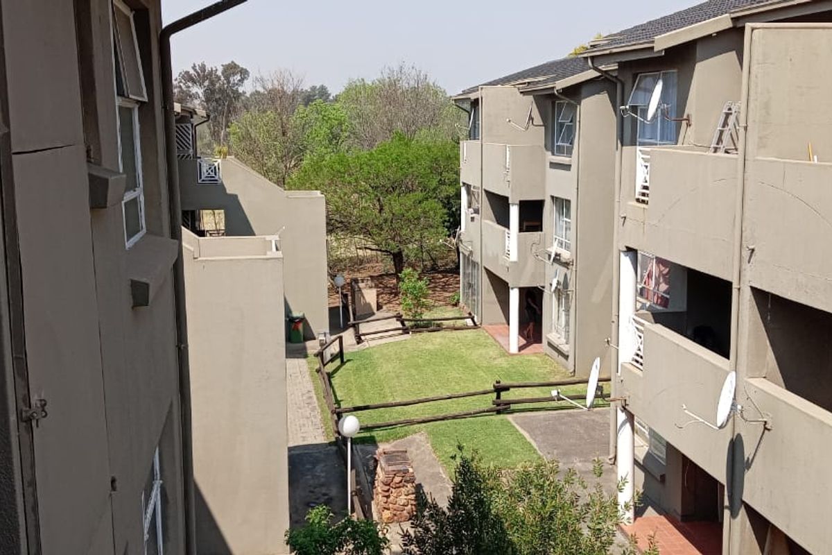 An elevated view of the apartment complex courtyard, featuring communal garden space, paved walkways, and private balconies with satellite dishes.