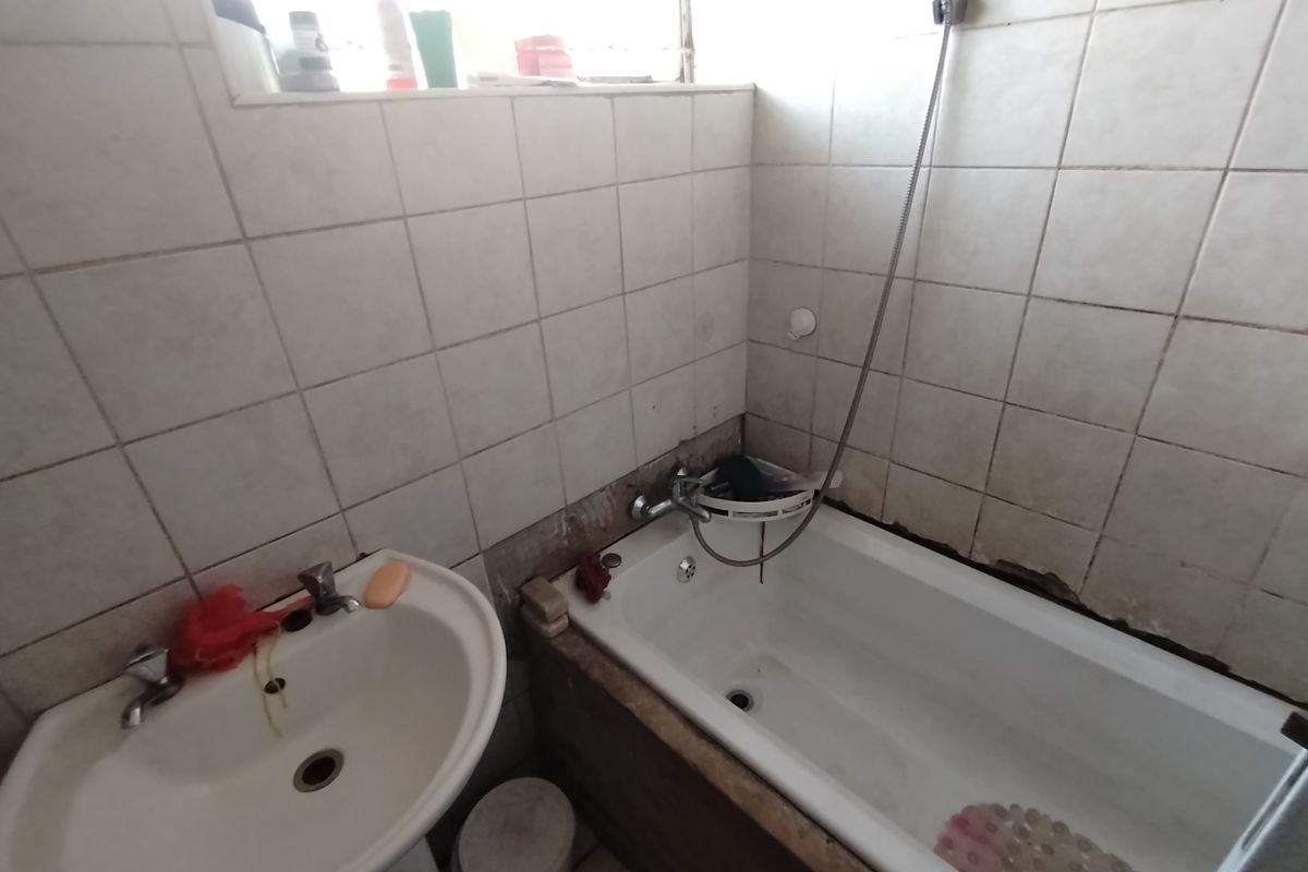 A functional bathroom featuring a pedestal basin and a standard bathtub with wall-mounted shower attachment and tiled splashbacks.