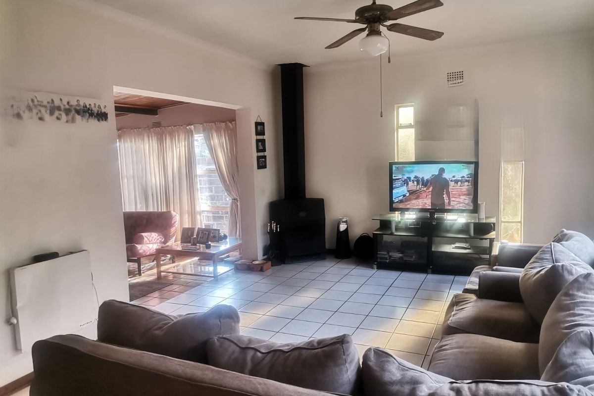 Spacious living room featuring tiled flooring, a built-in fireplace, and a ceiling fan, with an open-plan flow into an adjacent sunlit area.