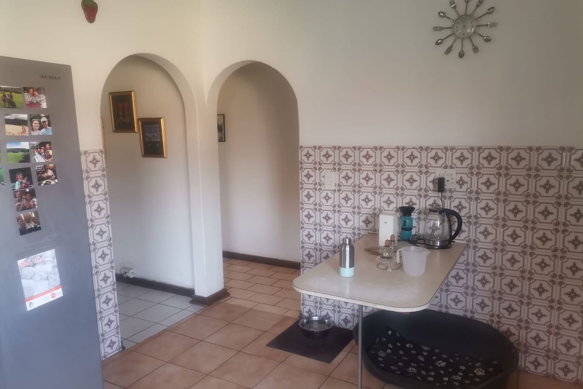 A functional kitchen area featuring arched doorways, patterned wall tiles, and a built-in breakfast counter, providing access to adjacent living spaces.