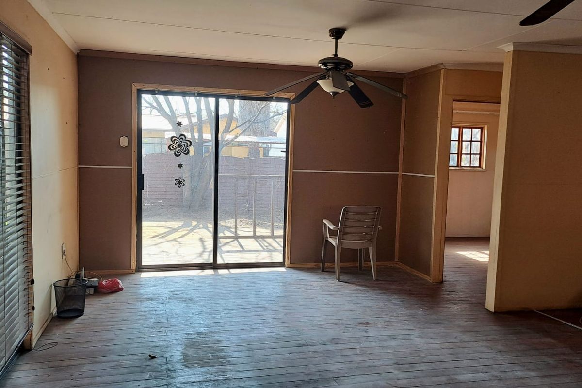 A living area featuring sliding glass doors leading to the exterior, a ceiling fan, and exposed flooring, offering a blank canvas for renovation.