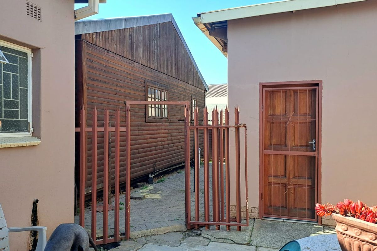 A side passage area featuring a timber-clad structure, paved walkway, and metal security gate between two building sections.