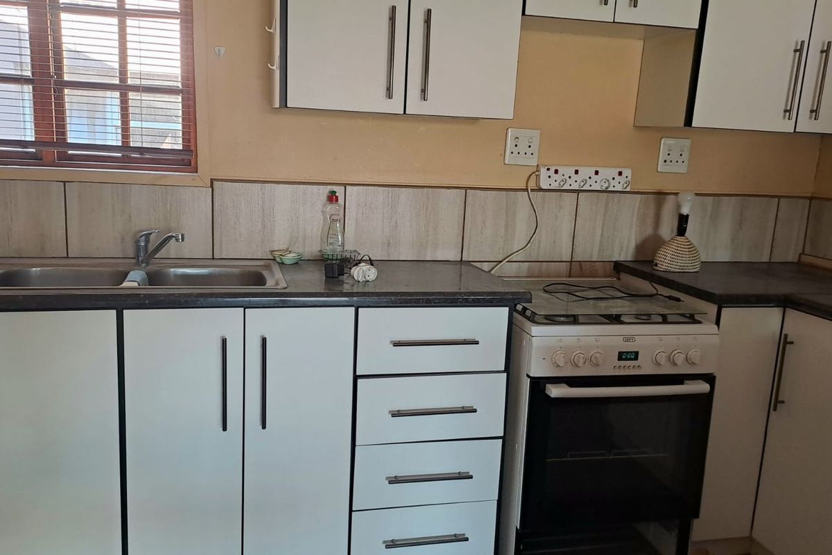 A functional kitchen featuring white cabinetry, a stainless steel sink, and a freestanding oven with a hob.