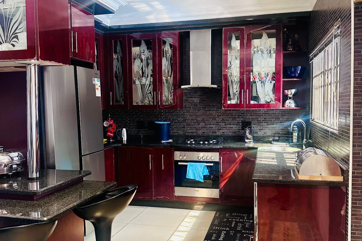 Modern kitchen featuring high-gloss burgundy cabinetry, granite countertops, stainless steel built-in oven, gas hob, and extractor fan with tiled flooring.