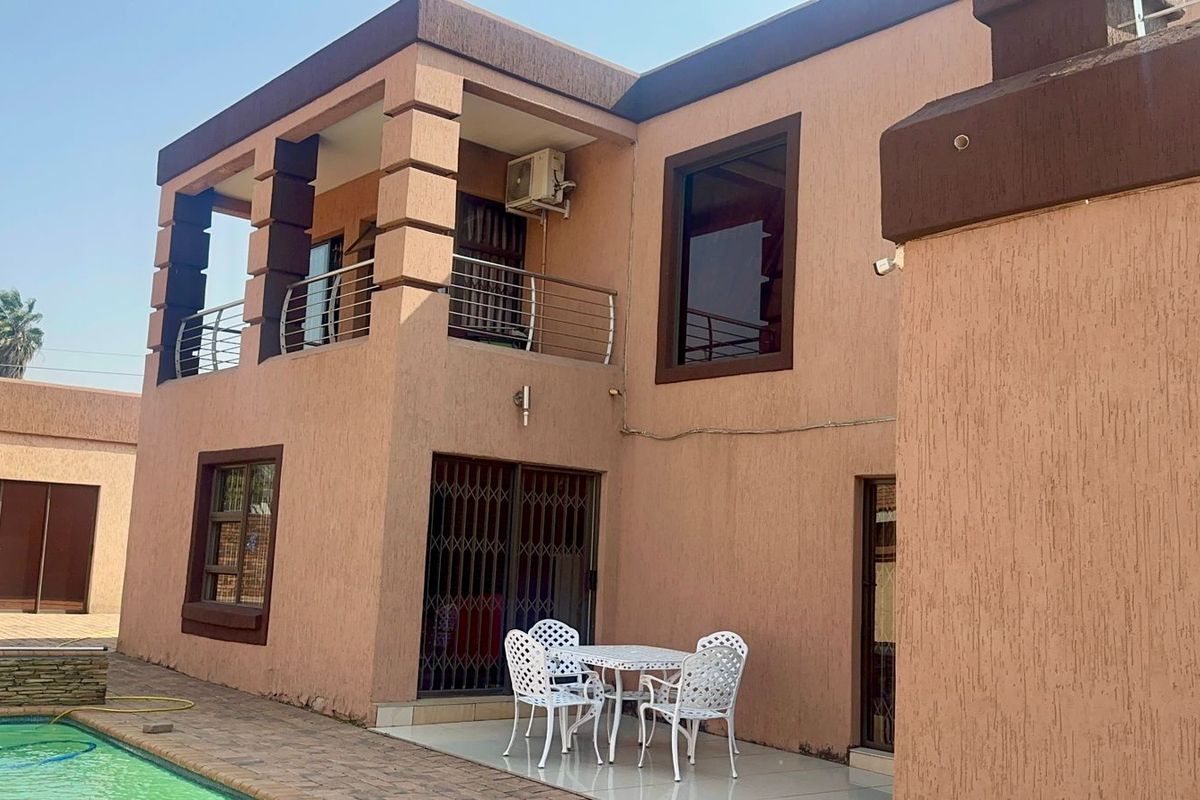 Rear view of a two-story house featuring a covered patio, balcony with stainless steel railings, and a swimming pool area.