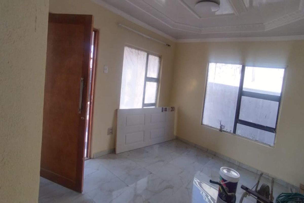 A bright, empty living room featuring tiled flooring, recessed ceiling detail, and large windows allowing for ample natural light.