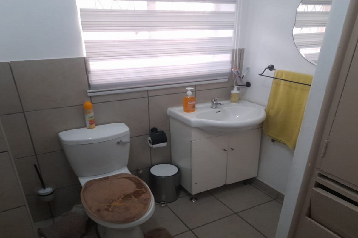 A functional bathroom featuring a white pedestal vanity, a standard toilet, and neutral wall tiling with a window providing natural light.