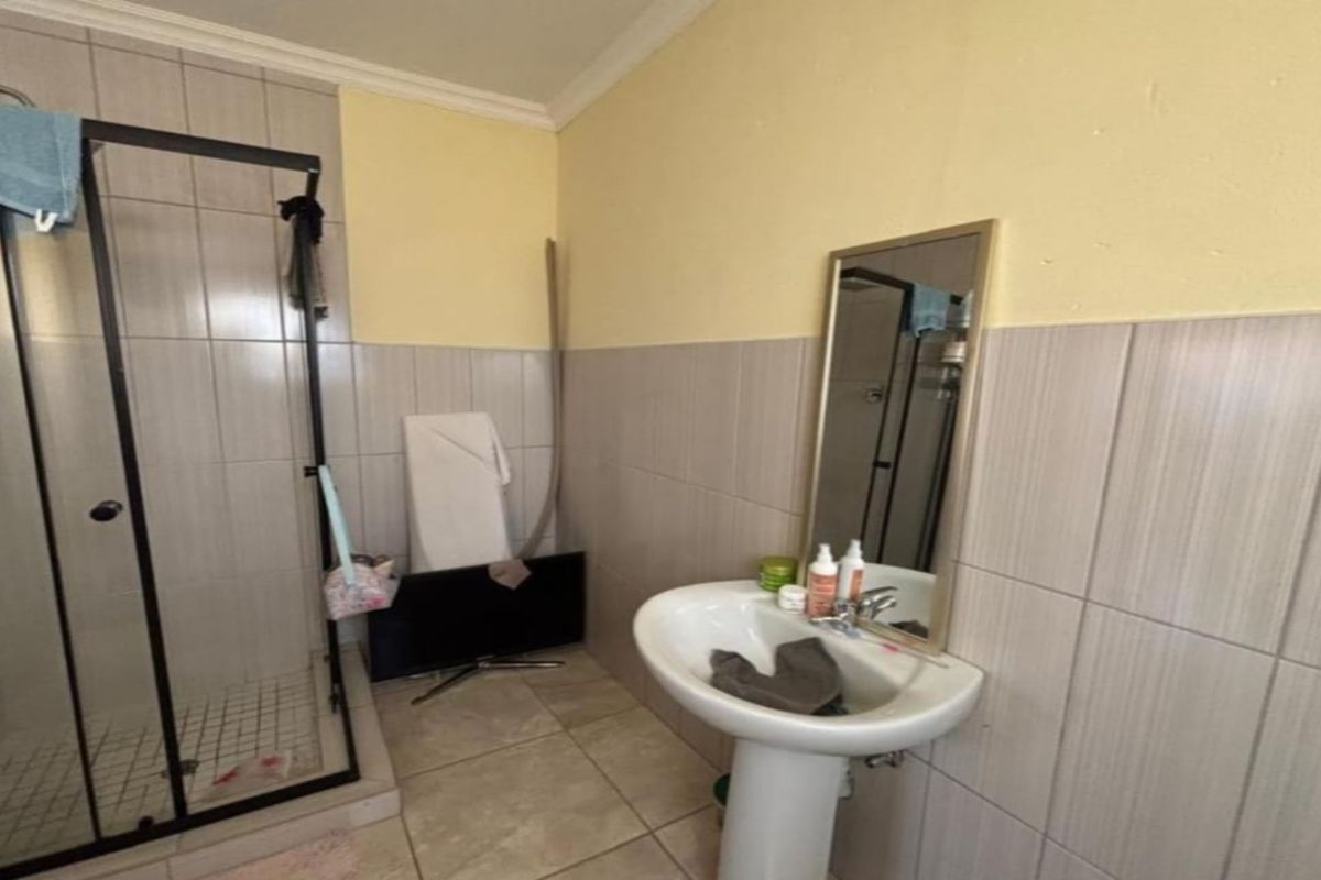 A functional bathroom featuring a glass-enclosed shower, a pedestal basin, and tiled wall finishes.