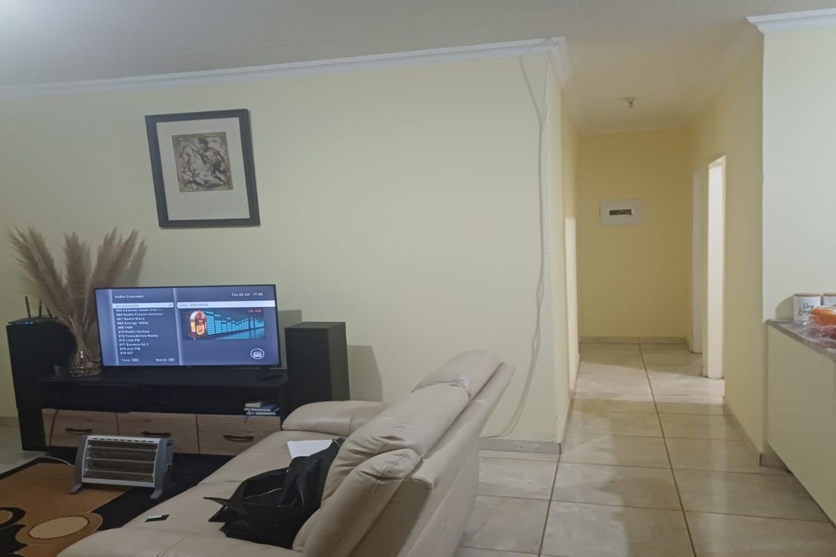 A living area featuring tiled flooring, crown molding, and an open-plan layout leading into a hallway.
