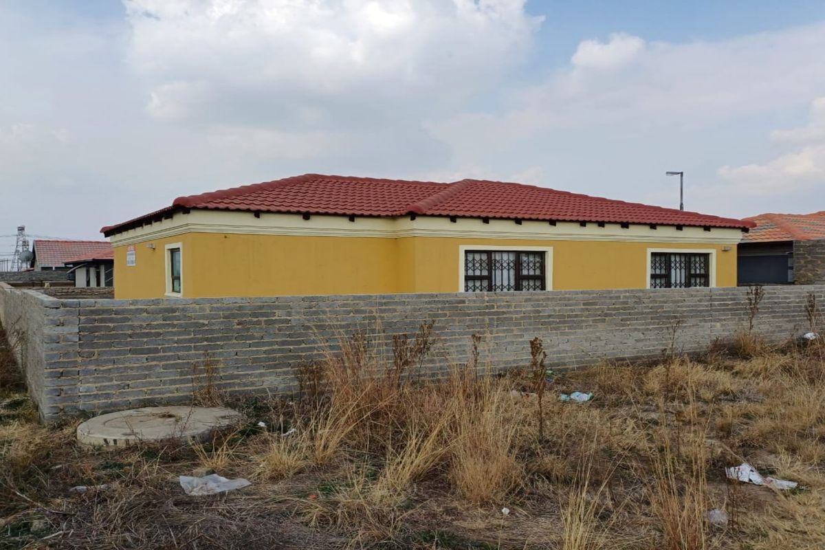 A side view of a single-story residential house featuring yellow exterior walls, a red tiled roof, and security bars on the windows.