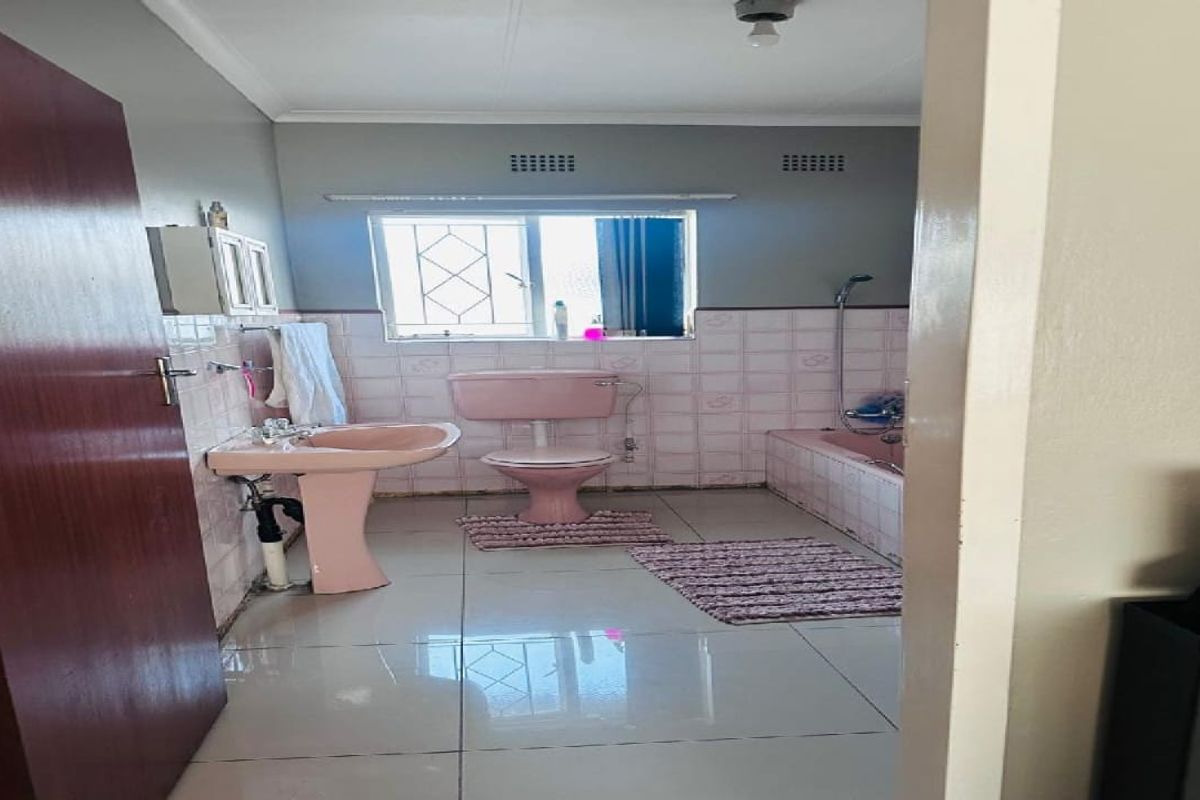 A dated bathroom featuring a vintage pink pedestal basin, matching toilet, and tiled bathtub with integrated shower fixtures.