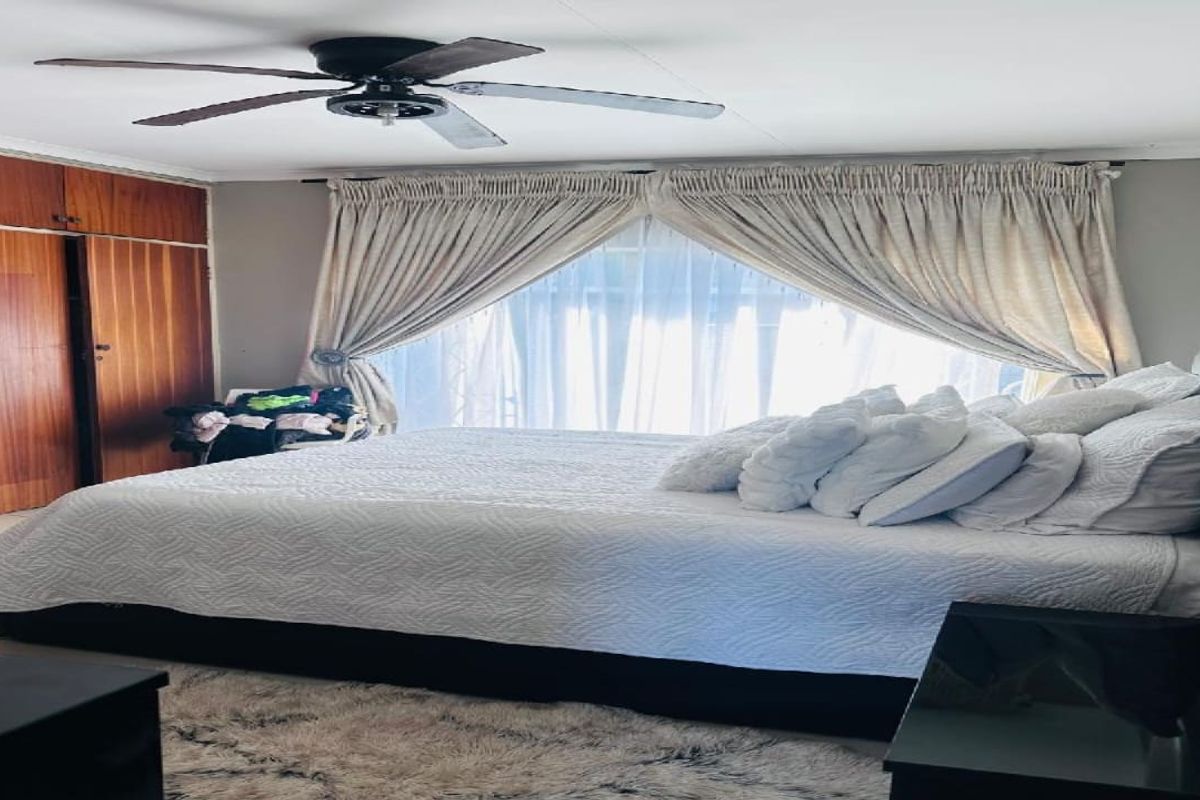 A bedroom featuring built-in wooden cupboards, a ceiling fan, and large windows with curtains.