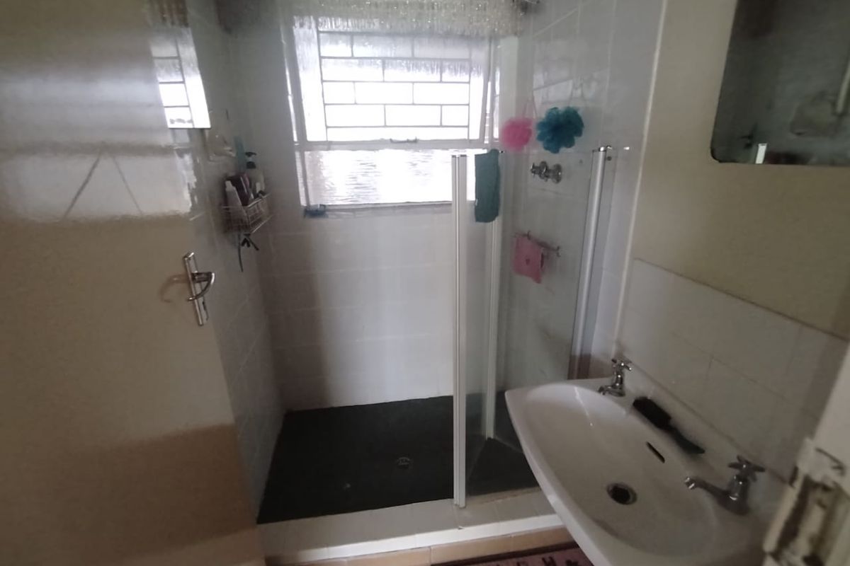 A functional bathroom featuring a walk-in shower with glass enclosure and a wall-mounted basin.