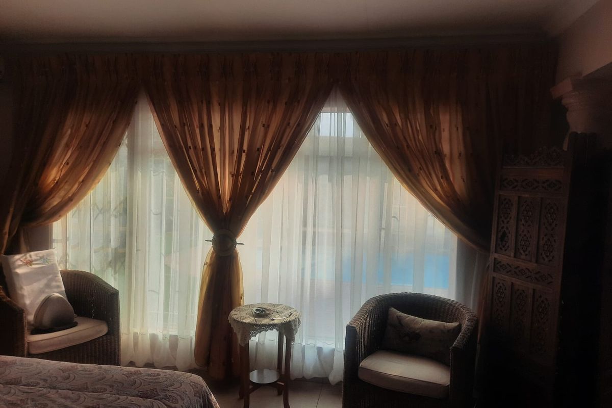 A bedroom featuring large windows with layered curtains, providing natural light and a view of the outdoor pool area.