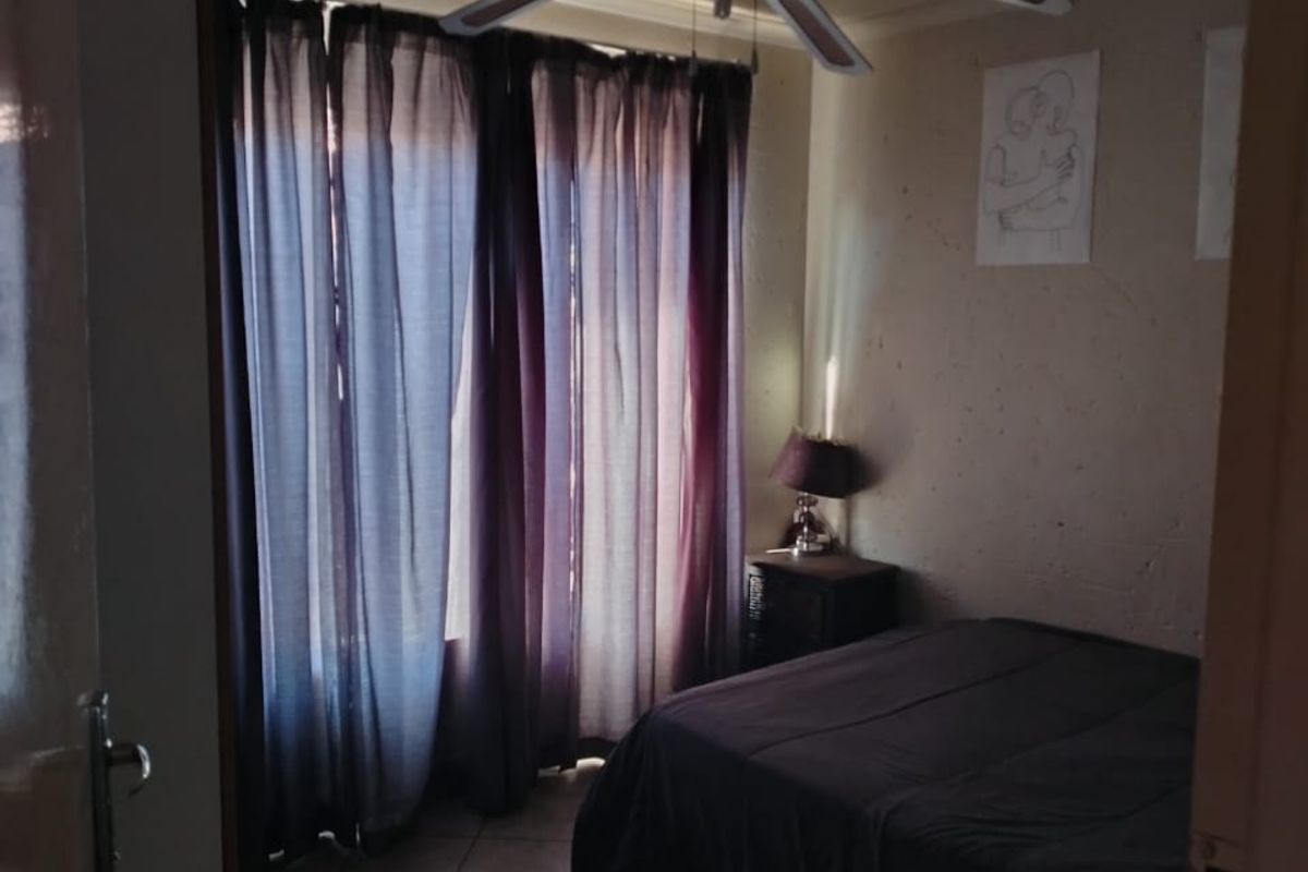 A bedroom featuring tiled flooring, a ceiling fan, and large windows with curtains, viewed from the doorway.