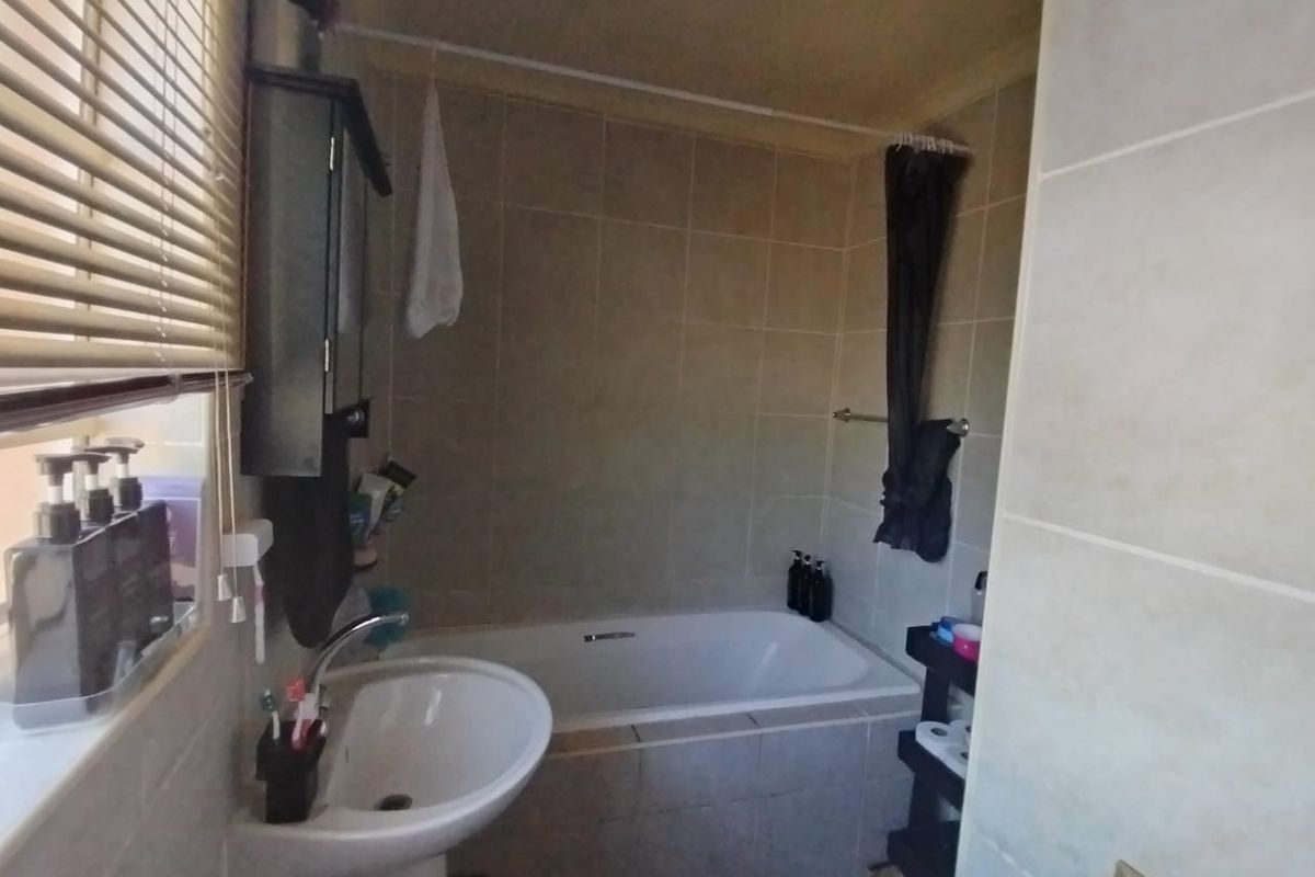 A functional bathroom featuring a pedestal basin, a tiled bathtub with shower curtain, and neutral wall tiling.