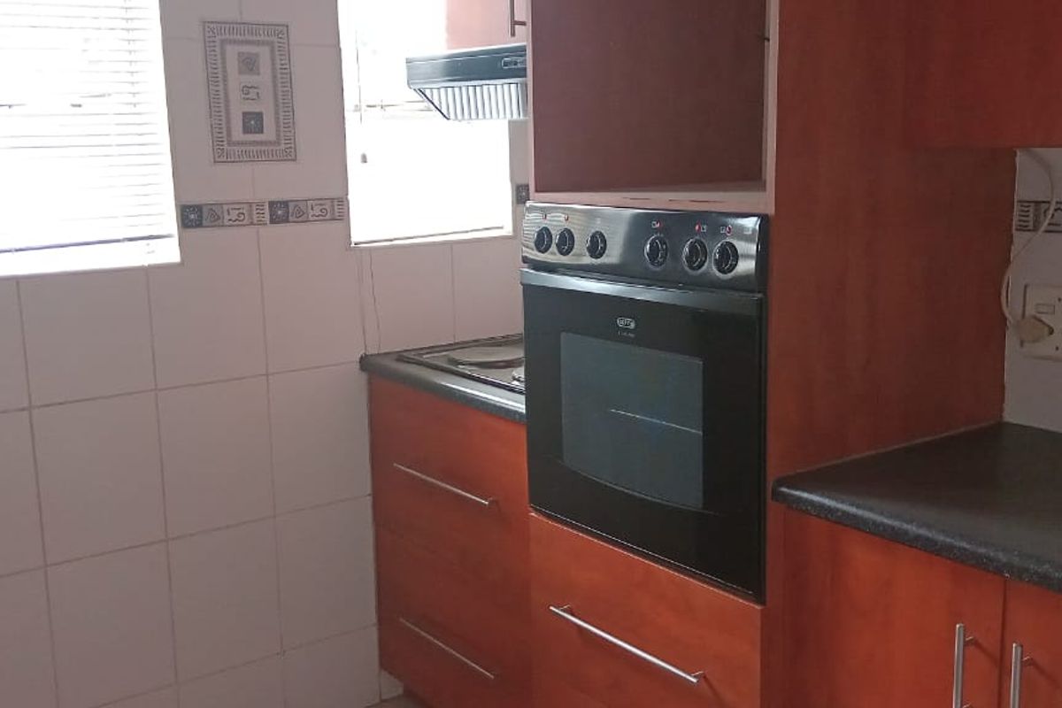 A functional kitchen featuring wood-finish cabinetry, a built-in oven, a hob, an extractor fan, and tiled wall splashbacks.