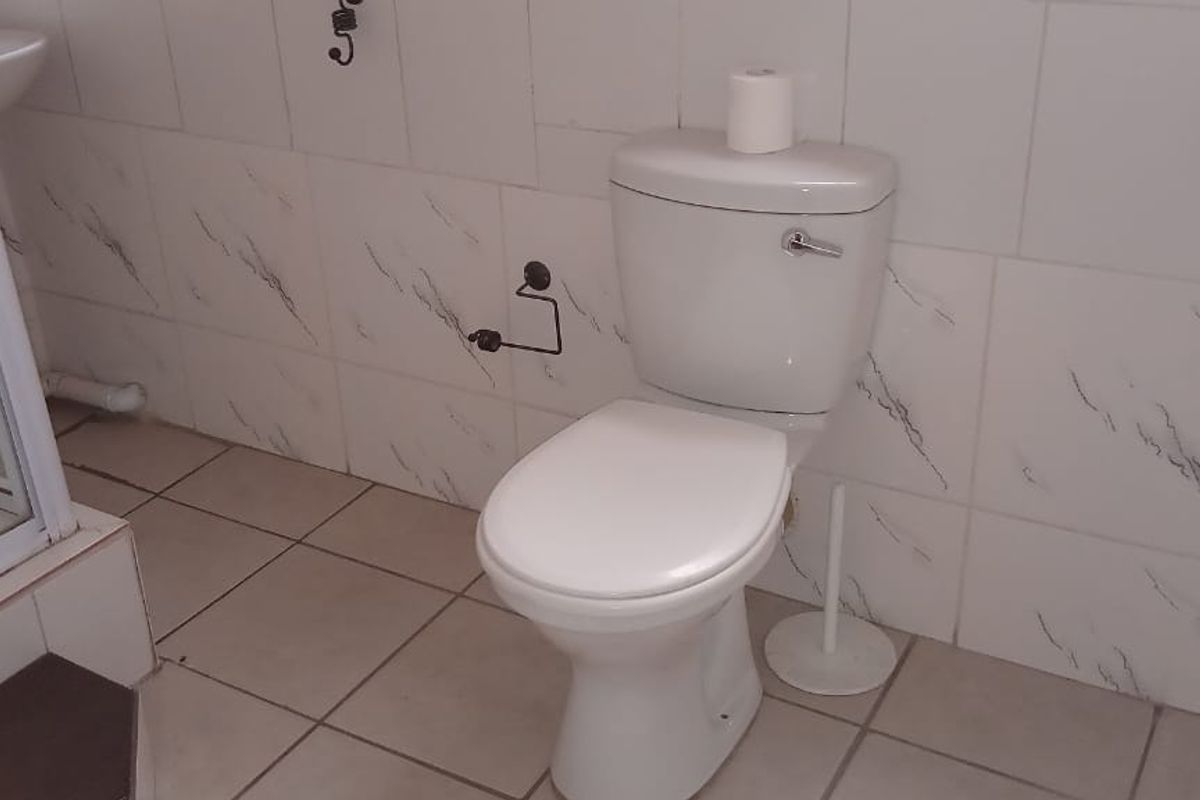 A functional bathroom featuring a standard toilet, pedestal basin, and a shower enclosure with tiled walls and flooring.