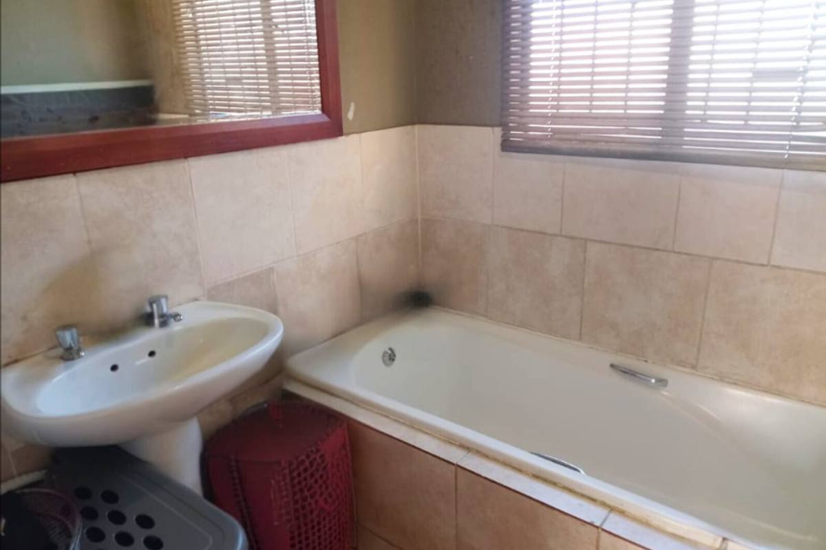 A functional bathroom featuring a built-in bathtub, pedestal basin, and wall-mounted mirror, requiring some maintenance and cosmetic updates.