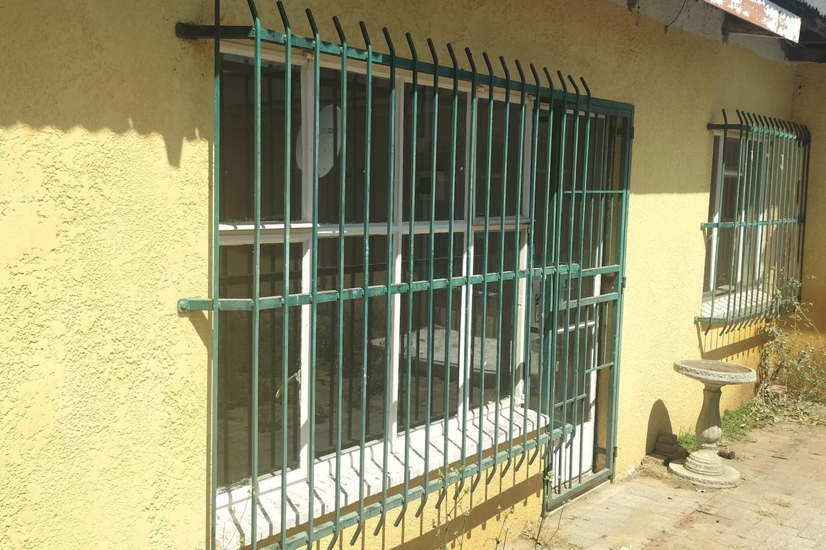 Exterior view of the property featuring yellow textured walls, security bars on windows, and a paved walkway area.