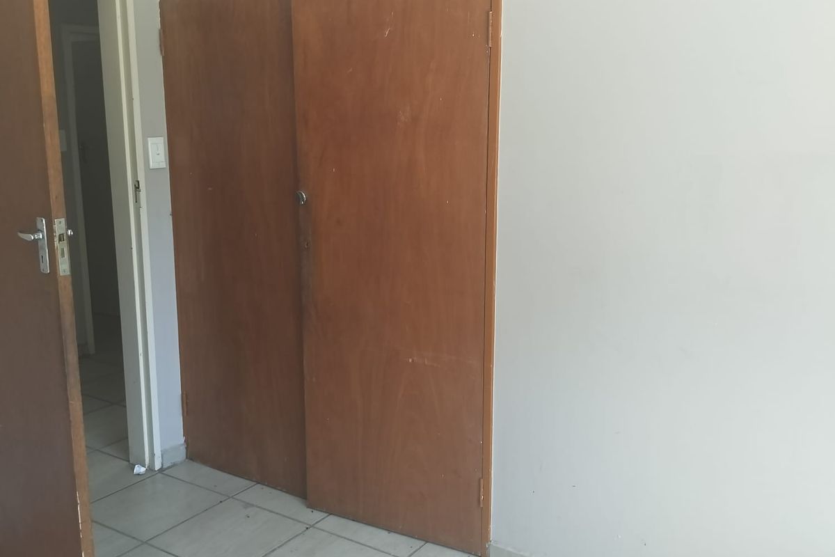 An empty bedroom featuring tiled flooring and a built-in wooden cupboard, requiring minor cosmetic updates.