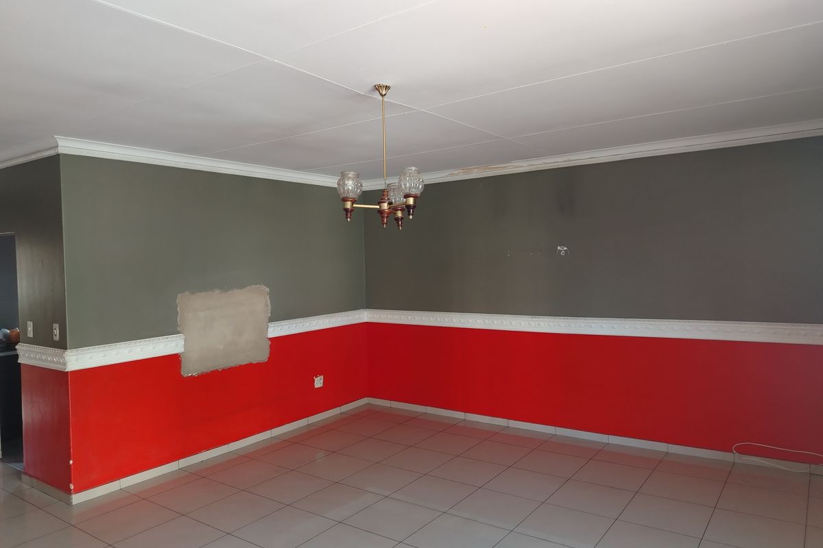 An empty living room featuring tiled flooring, decorative dado rails, and a central chandelier, currently requiring wall repairs and cosmetic updates.