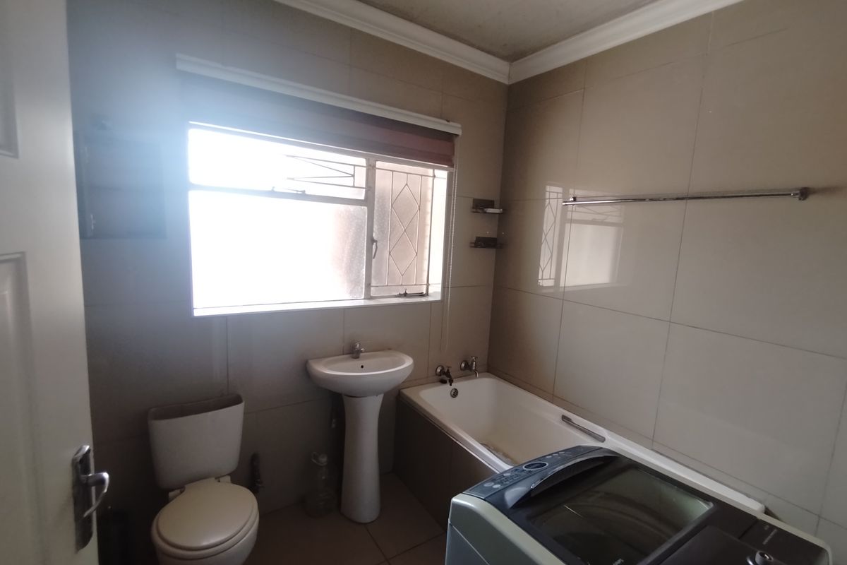 A functional bathroom featuring a pedestal basin, bathtub, and toilet, with tiled walls and a window for natural light.